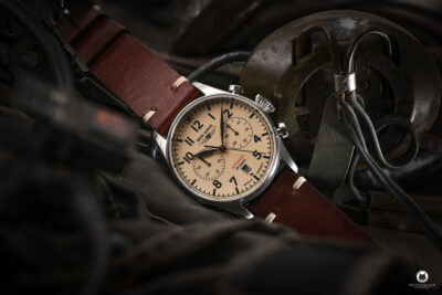 A vintage pilot watch with a cream dial and brown leather strap, resting on aviation gear, highlighting the connection between aviation and watch design