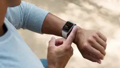A person wearing a smartwatch with a white strap, adjusting the display while seated outdoors, showcasing a stylish and functional accessory for any outfit