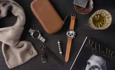 A stylish arrangement of watch accessories, including two watches, a leather case, a scarf, a tool, and a magazine, perfect for a wedding gift