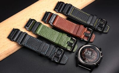 A variety of smartwatch straps in different colors and materials, including black, brown, green, and textured designs, displayed alongside a smartwatch on a dark surface