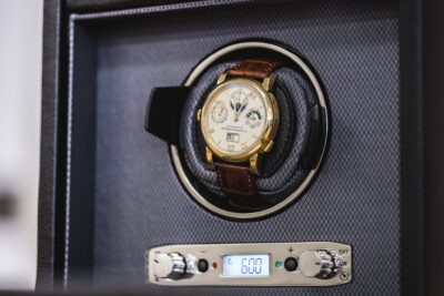 A close-up of a luxury watch resting in a watch winder, showcasing a manual and automatic winding mechanism with digital display settings
