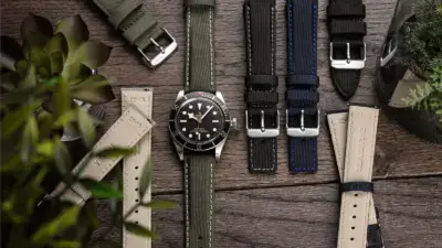 A stylish smartwatch surrounded by various watch straps in different colors and materials, set against a wooden background with greenery