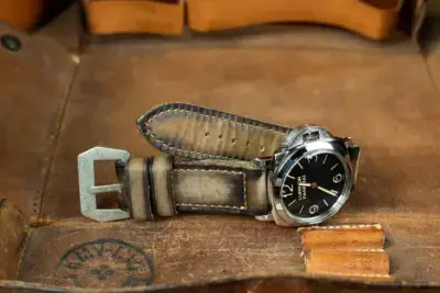 A vintage watch with a black dial and leather strap rests on a brown leather surface, showcasing a stylish accessory for elevating your look