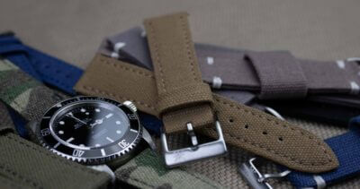 A close-up of various canvas and suede watch straps arranged around a black dive watch, highlighting their textures and colors for casual wear