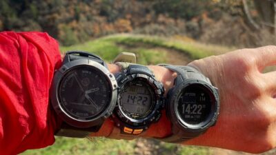 A close-up of a person's wrist showcasing three different waterproof watch bands, set against a scenic outdoor background, ideal for adventurers