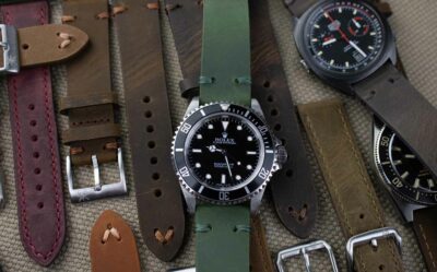 A collection of classic watch bracelets for men, featuring various styles and colors, including green and brown leather straps, displayed alongside a black dive watch