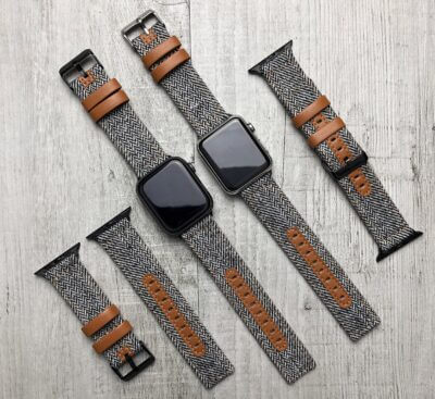A variety of smartwatch straps designed for active lifestyles, featuring a mix of herringbone fabric and leather accents, arranged on a wooden surface