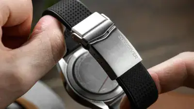 A close-up of a hand holding a watch with a deployant clasp, showcasing a sleek stainless steel finish and a textured black rubber strap