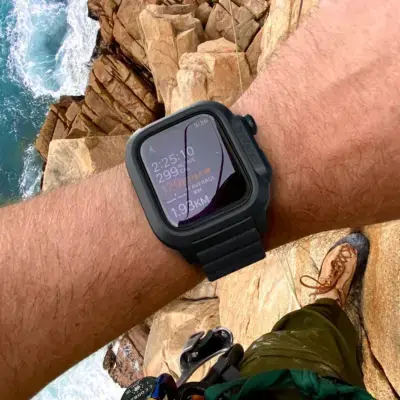 A close-up of a smartwatch on a person's wrist, showcasing its sleek design and protective case, with a rocky coastline and ocean in the background