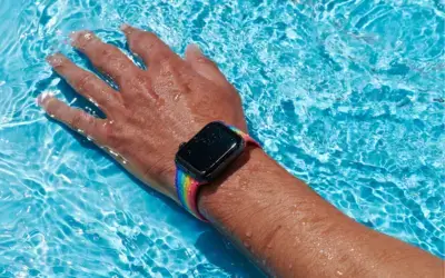 A hand with a colorful waterproof watch band submerged in clear blue water, illustrating the functionality and design of waterproof accessories