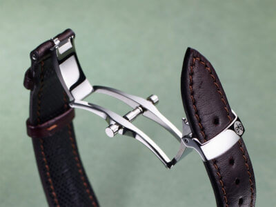 A close-up of a deployant clasp showcasing its sleek design and craftsmanship, featuring a polished metal finish and a leather watch strap