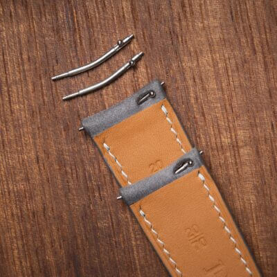 Close-up of a watch strap with two spring bars resting on a wooden surface, highlighting the innovative design elements that enhance watch customization and functionality