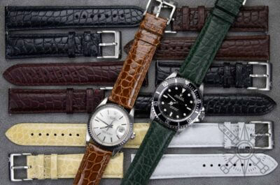A variety of crocodile and alligator watch straps in different colors, arranged alongside two watches, showcasing their versatility and style options
