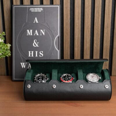 A stylish watch storage roll displaying three luxury watches, set against a wooden backdrop with a book titled "A Man & His Watches" nearby. Perfect for watch enthusiasts