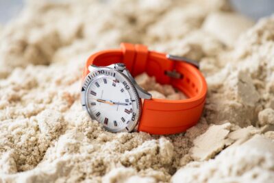 A modern watch with an orange FKM rubber band resting on sandy terrain, highlighting the durability and style of FKM rubber in contemporary watch design