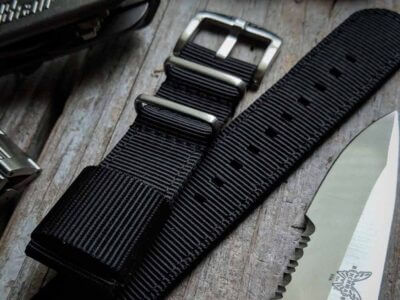 Close-up of a black quick release strap for a smartwatch, featuring a metal buckle and textured design, placed next to a knife on a rustic wooden surface