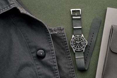 A black watch with a textured strap is displayed alongside a black jacket and a notebook, highlighting stylish options for active and outdoor lifestyles