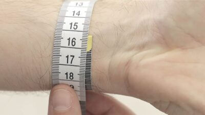A close-up of a hand measuring a wrist with a flexible measuring tape, highlighting the importance of accurate measurements for a perfect watch strap fit