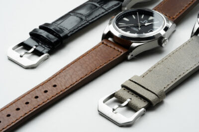 A close-up of three leather watch straps in black, brown, and gray, paired with silver watch cases, showcasing different textures and styles for watch enthusiasts
