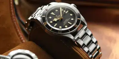 A close-up of a sleek metal watch with a black dial and luminous markers, resting on a soft leather surface, showcasing its polished shine and elegant design