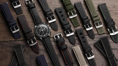 A variety of sailcloth watch straps in different colors and styles arranged around a classic watch on a wooden surface