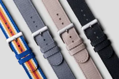 A collection of quick release straps in various colors, including blue with stripes, gray, beige, and black, displayed against a neutral background