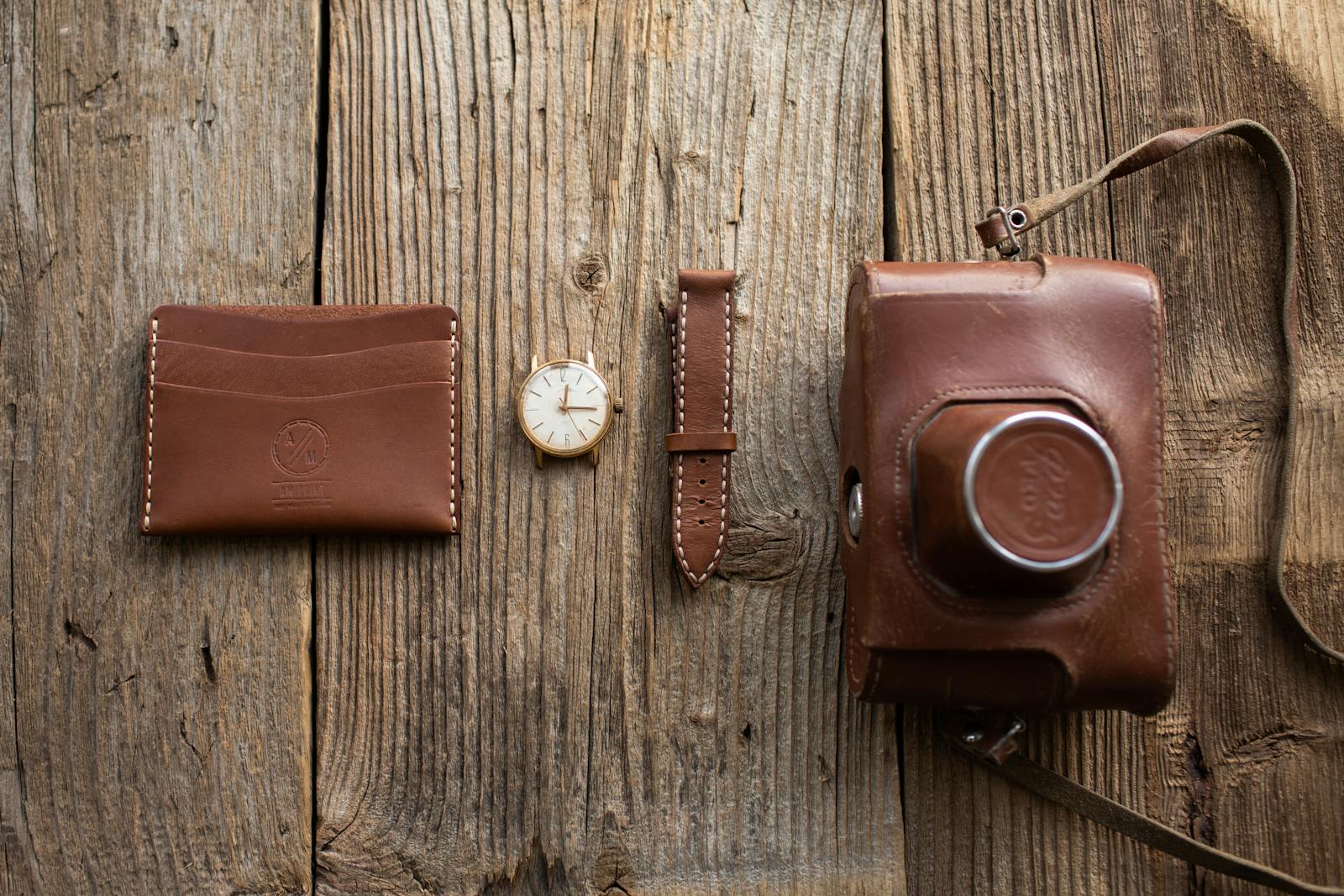 Close-up of leather wallet, watch, and camera case on wooden surface.