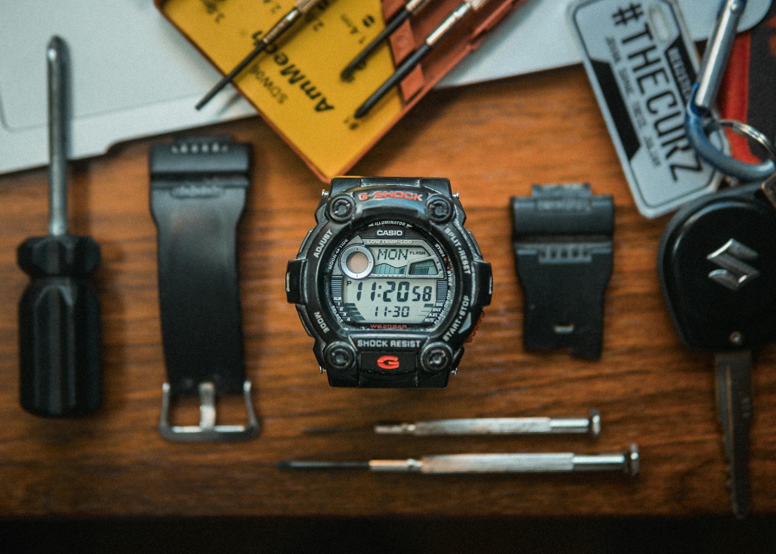 A flat lay photo showcasing a digital wristwatch and precision tools on a wooden surface.