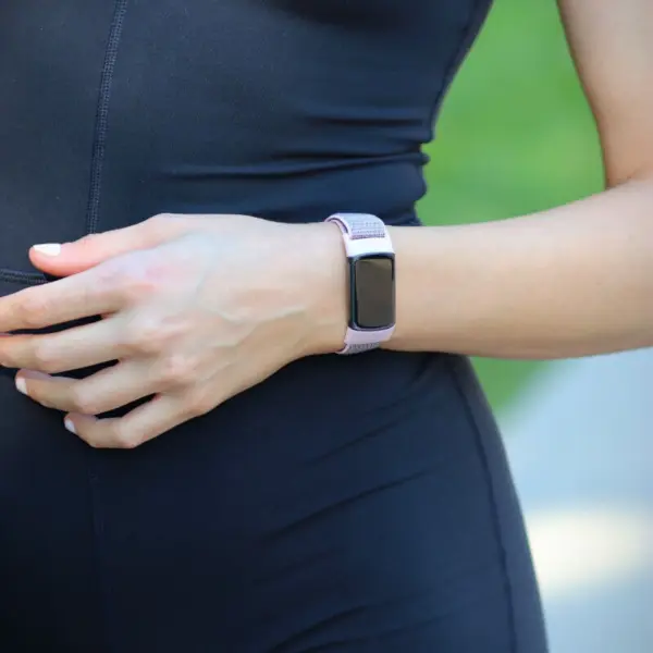 A close-up of a hand wearing the Everyday Nylon Strap for Fitbit Charge 5, showcasing its stylish design and comfortable fit against a backdrop of outdoor greenery