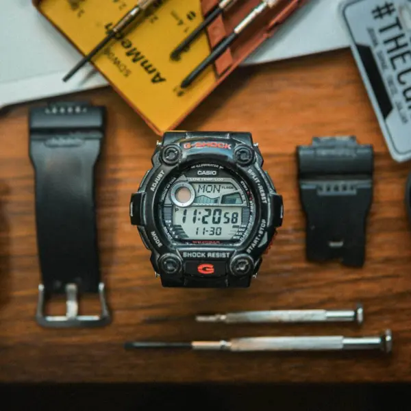 A flat lay photo showcasing a digital wristwatch and precision tools on a wooden surface.