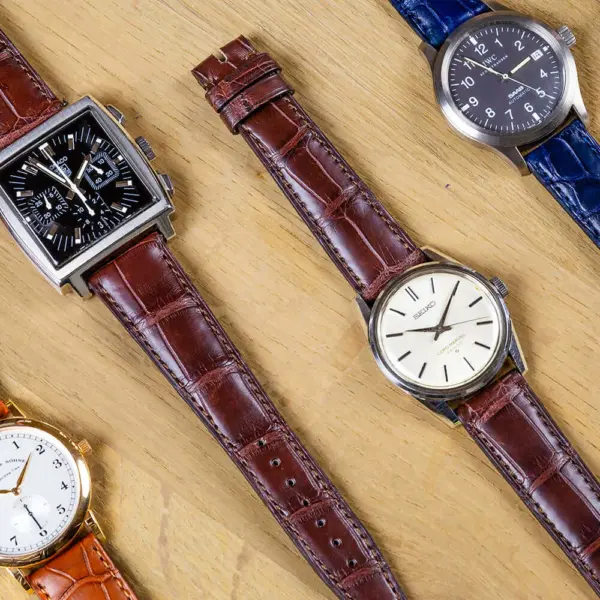 A collection of elegant watches featuring crocodile and alligator leather straps in various colors, showcasing their luxurious textures and designs on a wooden surface