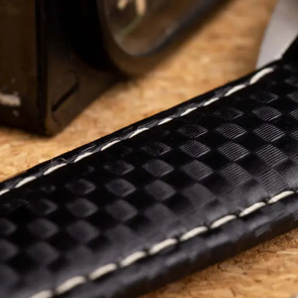 Close-up of a carbon watch strap on a textured surface, showcasing its unique pattern and stitching, ideal for a guide on cleaning and maintenance tips