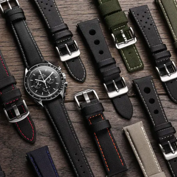 A variety of sailcloth watch straps in different colors and styles arranged around a classic watch on a wooden surface