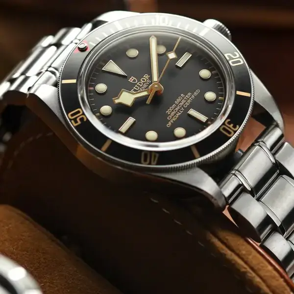 A close-up of a sleek metal watch with a black dial and luminous markers, resting on a soft leather surface, showcasing its polished shine and elegant design