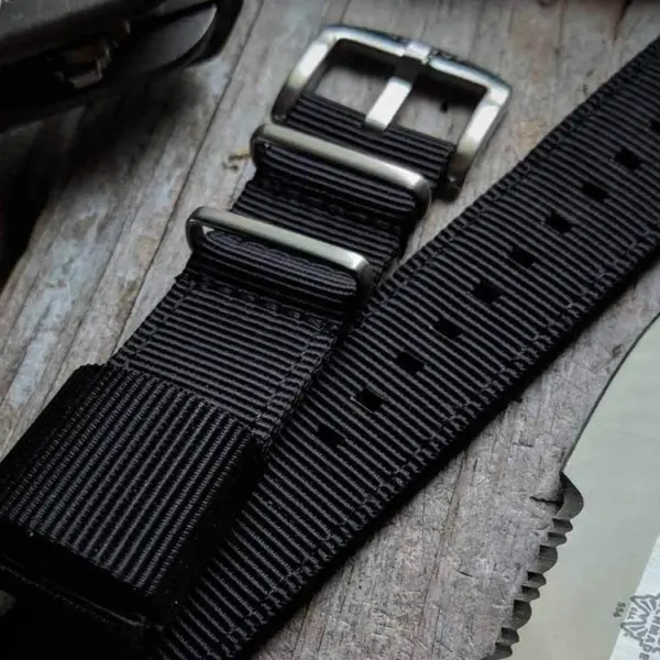 Close-up of a black quick release strap for a smartwatch, featuring a metal buckle and textured design, placed next to a knife on a rustic wooden surface