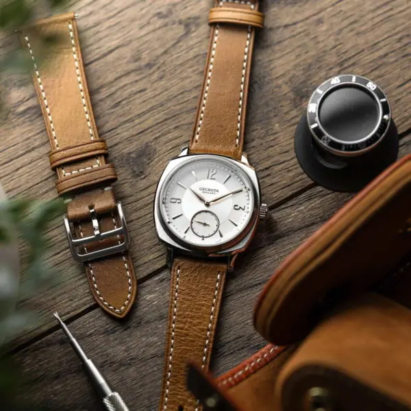 A stylish classic watch with a silver face and brown leather strap rests on a wooden surface, accompanied by an additional strap and watch tools, enhancing formal attire