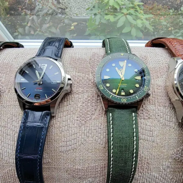 Four stylish watches with various strap colors displayed on a cushion by a window, showcasing options for casual weekend wear