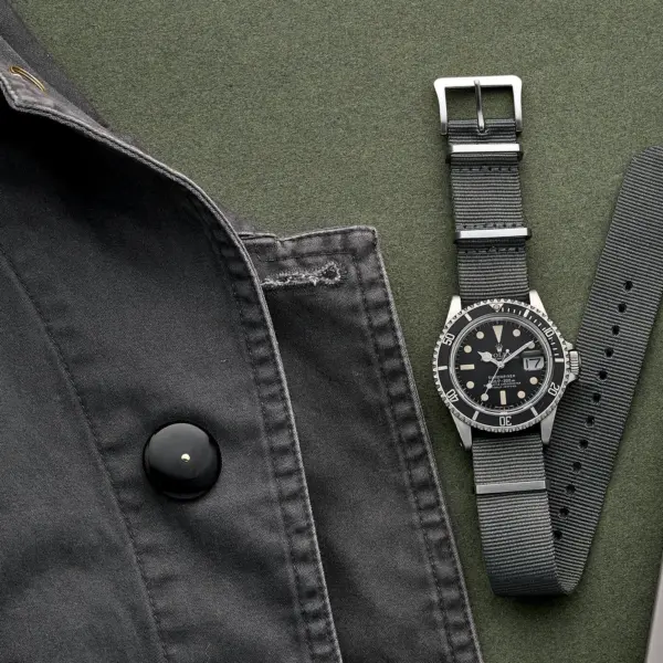 A black watch with a textured strap is displayed alongside a black jacket and a notebook, highlighting stylish options for active and outdoor lifestyles