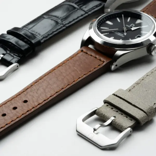 A close-up of three leather watch straps in black, brown, and gray, paired with silver watch cases, showcasing different textures and styles for watch enthusiasts