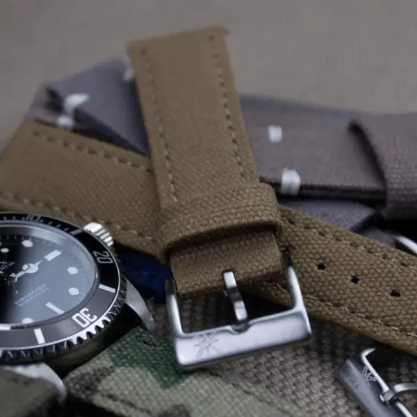 A close-up of various canvas and suede watch straps arranged around a black dive watch, highlighting their textures and colors for casual wear