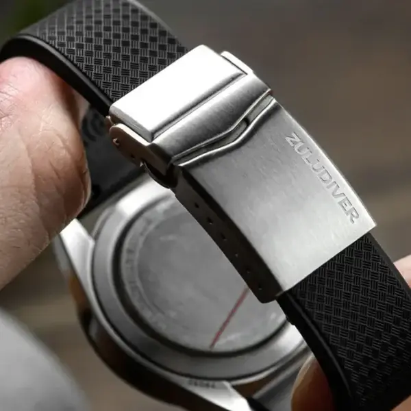 A close-up of a hand holding a watch with a deployant clasp, showcasing a sleek stainless steel finish and a textured black rubber strap