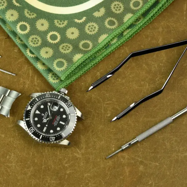 A watch, spring bars, tweezers, and a screwdriver are arranged on a textured surface, highlighting essential tools for watch maintenance and care