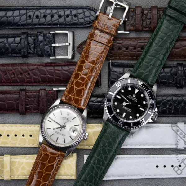 A variety of crocodile and alligator watch straps in different colors, arranged alongside two watches, showcasing their versatility and style options