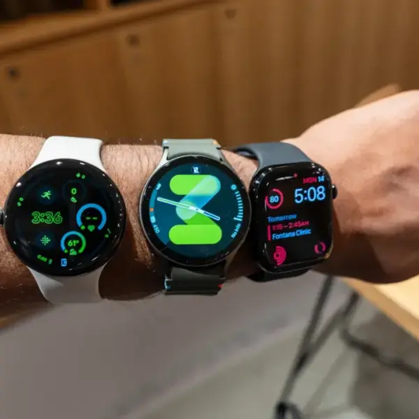 Three smartwatches with different straps displayed on a person's wrist, showcasing various designs and features against a wooden background