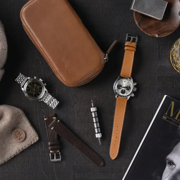 A stylish arrangement of watch accessories, including two watches, a leather case, a scarf, a tool, and a magazine, perfect for a wedding gift