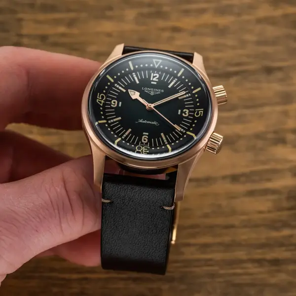 A hand holding a stylish watch with a black strap and a sleek, dark dial, set against a rustic wooden background, perfect for wedding-ready accessories