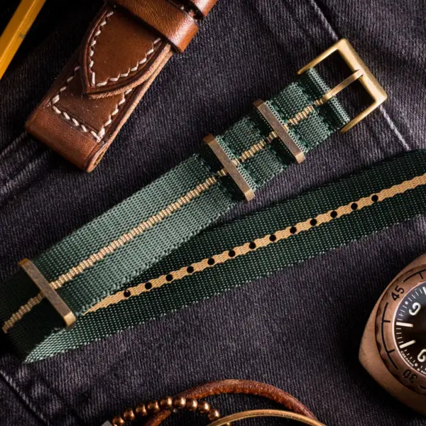 A collection of stylish watch bands laid out on denim, featuring a green fabric band with gold accents, alongside leather bands and a classic watch