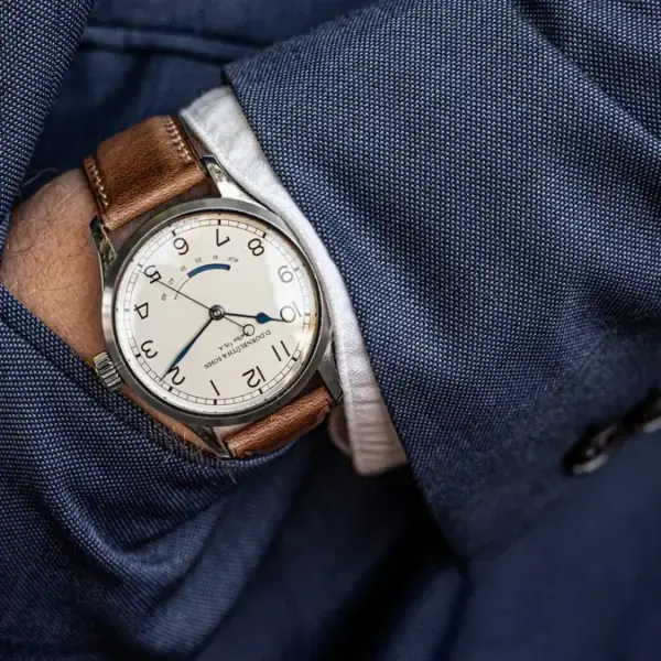 A close-up of a stylish watch with a brown leather band peeking out from a tailored blue suit jacket, showcasing elegance suitable for a formal event