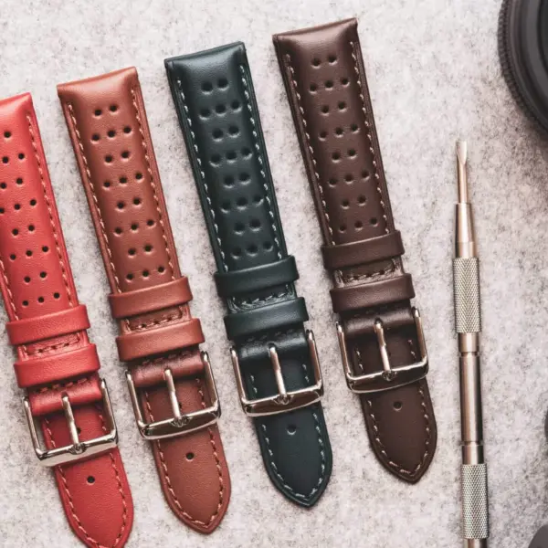 Four stylish watch straps in red, green, brown, and dark brown laid out on a textured surface, alongside a camera, notebook, and pen, perfect for office accessorizing