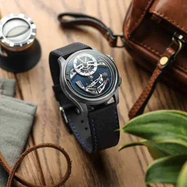 A stylish watch with a blue strap is placed on a wooden surface alongside a brown leather bag, a measuring tool, and a green plant, showcasing a blend of elegance and practicality